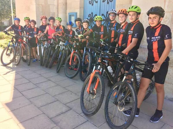 kinderen staan in de rij met fietsen in zwarte en oranje wielertruien