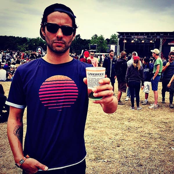 homme à un festival avec des lunettes de soleil portant un tshirt violet avec coucher de soleil