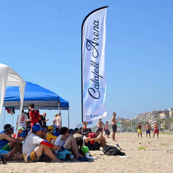white calafell beach flag with people sitting on beach