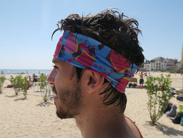 left side view of head of man wearing a pink and blue headband at the beach
