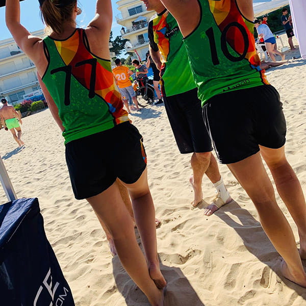 thumbnail rear view of women on beach under a tent wearing colorful jerseys and short black shorts