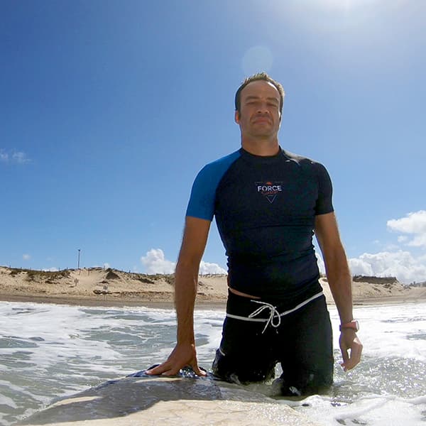 man in the ocean with black and blue rash vest and surfboard